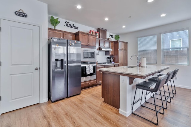 915 Winchell Way W, Madera, CA 93636 - kitchen with appliances with stainless steel finishes, under cabinet range hood, a kitchen island with sink, a kitchen breakfast bar, and light wood-style flooring