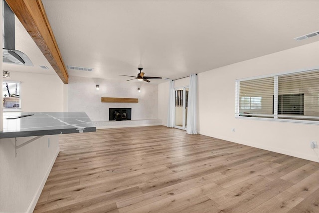 652 E Portals Ave, Fresno, CA 93710 - unfurnished living room featuring a ceiling fan, wood finished floors, a fireplace with raised hearth, and plenty of natural light