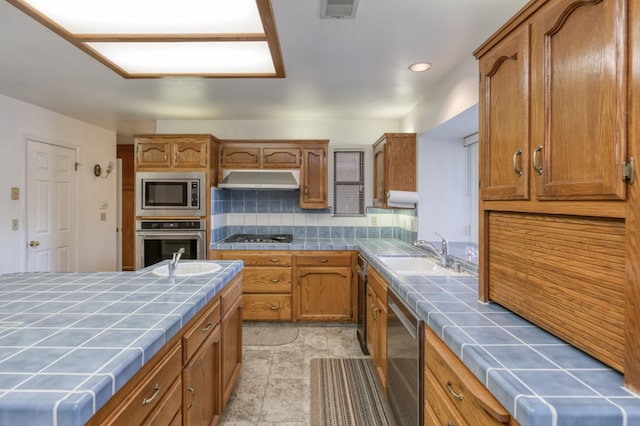7664 N Kavanagh Ave, Fresno, CA 93711 - kitchen featuring tile counters, appliances with stainless steel finishes, under cabinet range hood, brown cabinetry, and recessed lighting