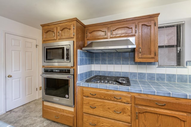 7664 N Kavanagh Ave, Fresno, CA 93711 - kitchen featuring stainless steel appliances, tile counters, ventilation hood, and brown cabinets