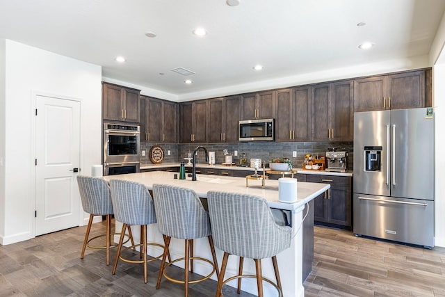 2421 N Cabrenet Pl, Hanford, CA 93230 - kitchen with appliances with stainless steel finishes, dark brown cabinets, light countertops, backsplash, and a kitchen breakfast bar