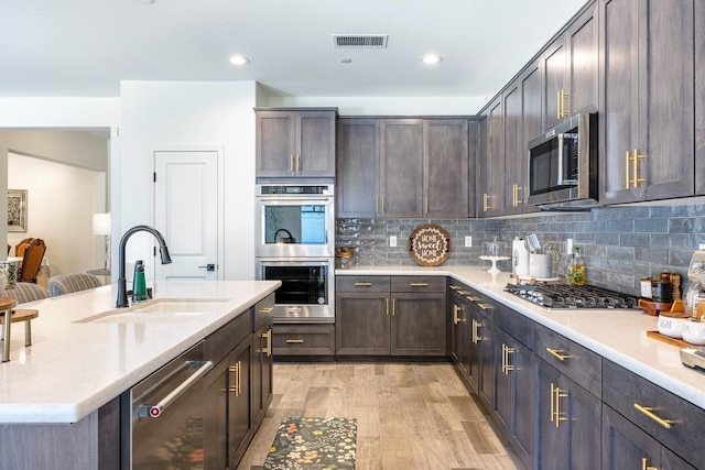 2421 N Cabrenet Pl, Hanford, CA 93230 - kitchen with stainless steel appliances, light wood-style flooring, decorative backsplash, dark brown cabinets, and an island with sink