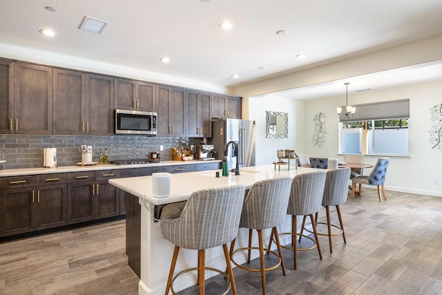 2421 N Cabrenet Pl, Hanford, CA 93230 - kitchen with stainless steel appliances, a kitchen breakfast bar, light countertops, light wood finished floors, and a kitchen island with sink
