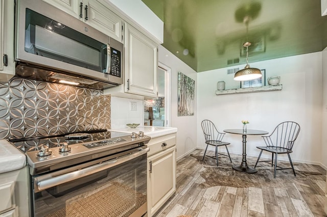 5180 N Wishon Ave Unit 103, Fresno, CA 93704 - kitchen featuring appliances with stainless steel finishes, light wood-style floors, decorative backsplash, light countertops, and pendant lighting