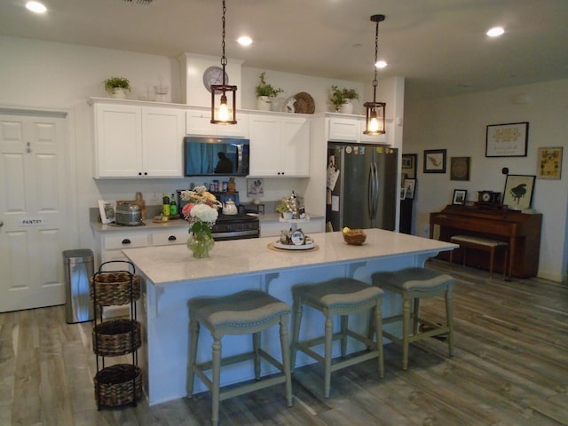 6908 E Castle Ave, Fresno, CA 93727 - kitchen with appliances with stainless steel finishes, dark wood-style floors, white cabinetry, a kitchen breakfast bar, and light countertops