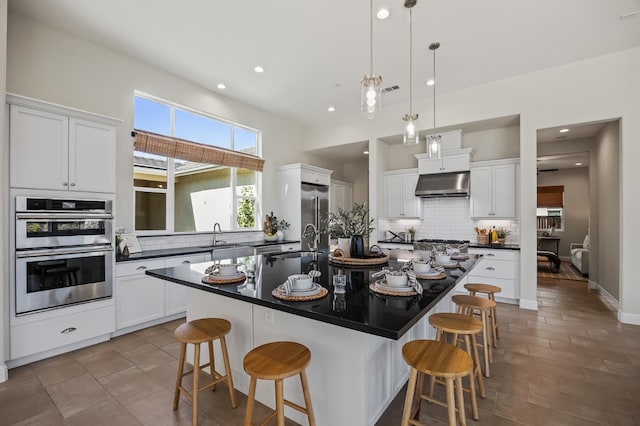 998 Highland Rd W, Madera, CA 93636 - kitchen with under cabinet range hood, appliances with stainless steel finishes, dark countertops, a kitchen bar, and decorative backsplash