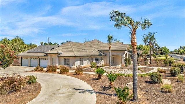 431 S Fowler Ave, Fresno, CA 93727 - view of front of property featuring curved driveway, roof mounted solar panels, an attached garage, stucco siding, and a tiled roof