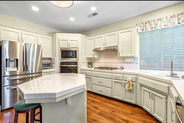 4632 W Minarets Ave, Fresno, CA 93722 - kitchen with appliances with stainless steel finishes, tile counters, under cabinet range hood, decorative backsplash, and dark wood-type flooring