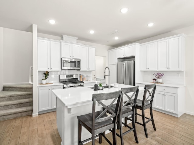 6274 E Riesling Dr, Fresno, CA 93727 - kitchen featuring stainless steel appliances, light wood-type flooring, light countertops, an island with sink, and backsplash