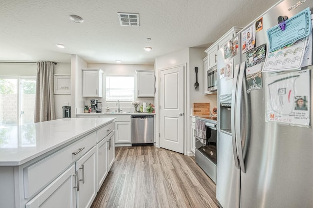2012 Richard Ave, Sanger, CA 93657 - kitchen featuring stainless steel appliances, light wood-style floors, light countertops, white cabinets, and a textured ceiling