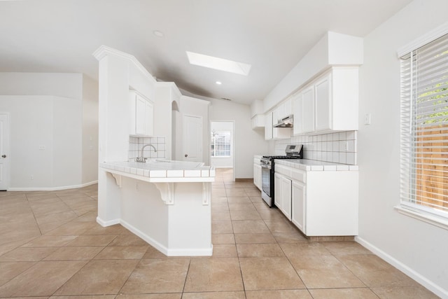 5647 N Tracy Ave, Fresno, CA 93722 - kitchen featuring stainless steel range with gas stovetop, tile counters, backsplash, a skylight, and lofted ceiling