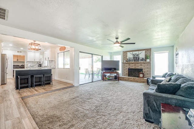 3377 N Bryan Ave, Fresno, CA 93723 - living area featuring a brick fireplace, a textured ceiling, light wood-type flooring, and a ceiling fan