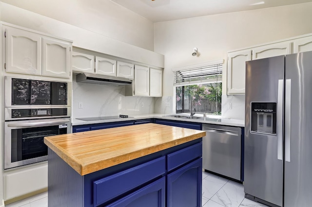6447 N Vagedes Ave, Fresno, CA 93711 - kitchen with stainless steel appliances, blue cabinets, under cabinet range hood, wooden counters, and decorative backsplash