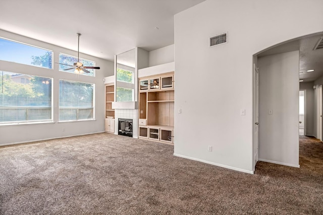 5811 W Beechwood Ave, Fresno, CA 93722 - unfurnished living room with carpet floors, a ceiling fan, arched walkways, a fireplace, and a towering ceiling