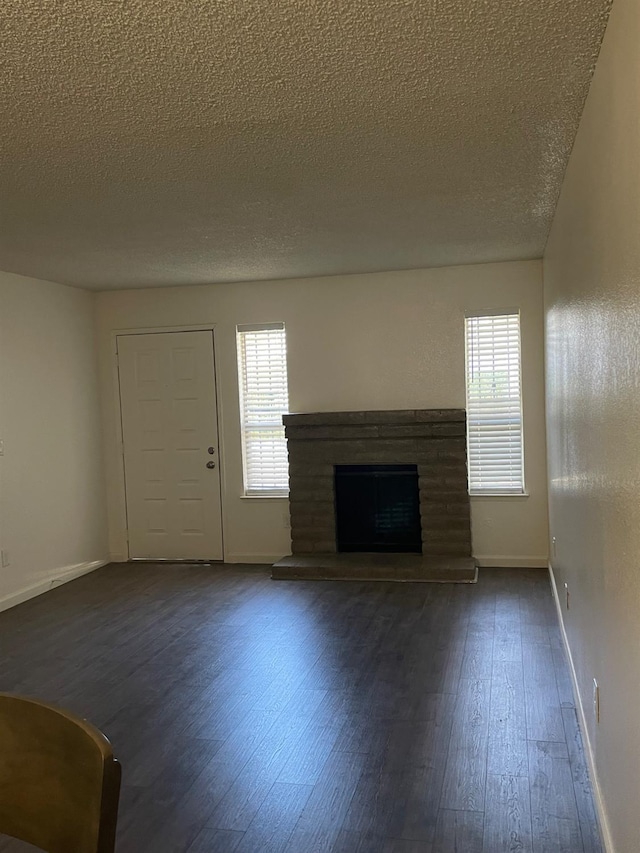 1027 W Dakota Ave Unit 102, Fresno, CA 93705 - unfurnished living room featuring a textured ceiling, dark wood-style flooring, a fireplace with raised hearth, and plenty of natural light