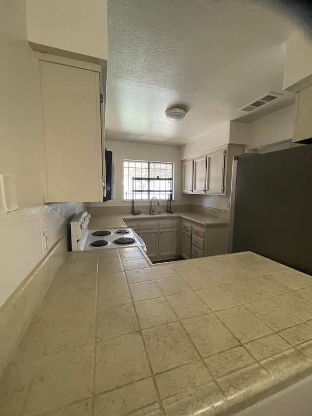 1027 W Dakota Ave Unit 102, Fresno, CA 93705 - kitchen with white electric stove, freestanding refrigerator, a textured ceiling, and tile counters