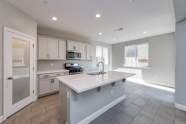 7393 E Michigan Ave, Fresno, CA 93737 - kitchen with appliances with stainless steel finishes, a center island with sink, light countertops, a kitchen bar, and decorative backsplash