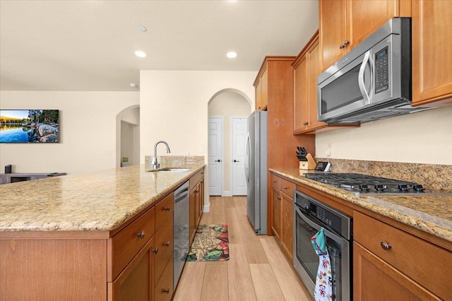 2481 S Via Versilia Dr, Fresno, CA 93727 - kitchen featuring appliances with stainless steel finishes, arched walkways, light wood-style flooring, brown cabinetry, and light stone counters