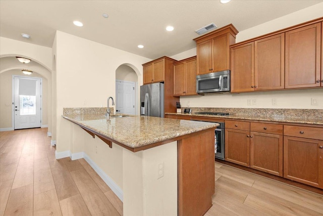2481 S Via Versilia Dr, Fresno, CA 93727 - kitchen with stainless steel appliances, arched walkways, brown cabinetry, light stone countertops, and a peninsula
