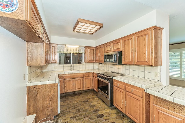 10465 E Herndon Ave, Clovis, CA 93619 - kitchen featuring appliances with stainless steel finishes, tasteful backsplash, tile counters, dark stone finish flooring, and brown cabinetry