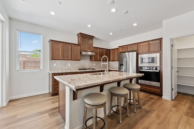 1567 Las Rosas Ave, Clovis, CA 93619 - kitchen with appliances with stainless steel finishes, backsplash, light wood-style flooring, an island with sink, and under cabinet range hood