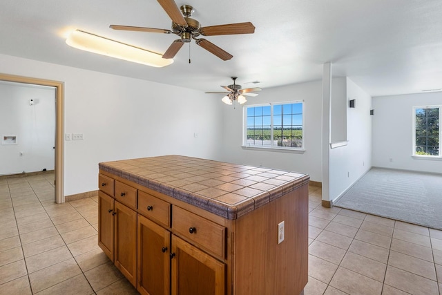 570 S Lassen Ave, Kerman, CA 93630 - kitchen with tile countertops, light tile patterned floors, brown cabinetry, a ceiling fan, and a center island