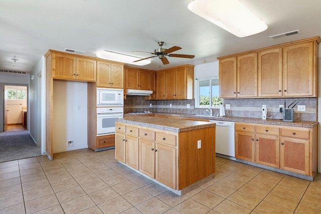 570 S Lassen Ave, Kerman, CA 93630 - kitchen featuring white appliances, under cabinet range hood, light tile patterned floors, decorative backsplash, and a kitchen island
