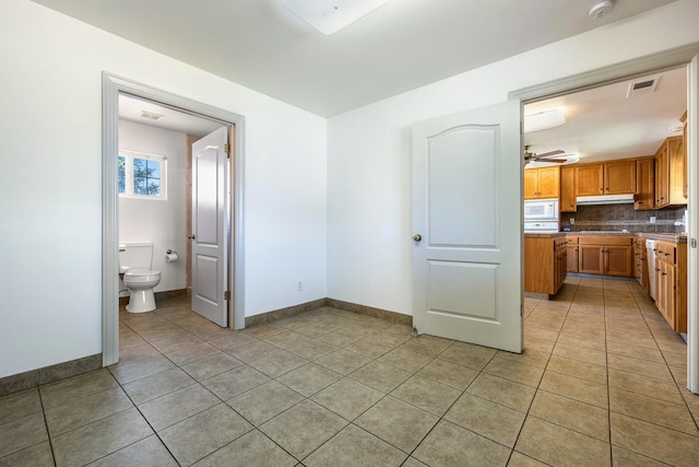 570 S Lassen Ave, Kerman, CA 93630 - kitchen with light tile patterned floors, white microwave, a ceiling fan, under cabinet range hood, and backsplash