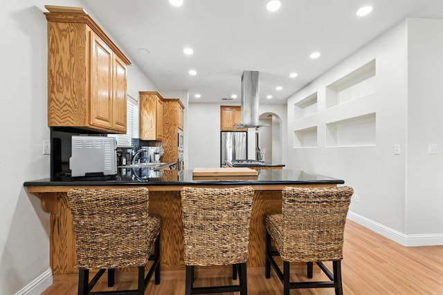 135 N Park Dr, Madera, CA 93637 - kitchen with island exhaust hood, a peninsula, dark countertops, light wood-type flooring, and recessed lighting