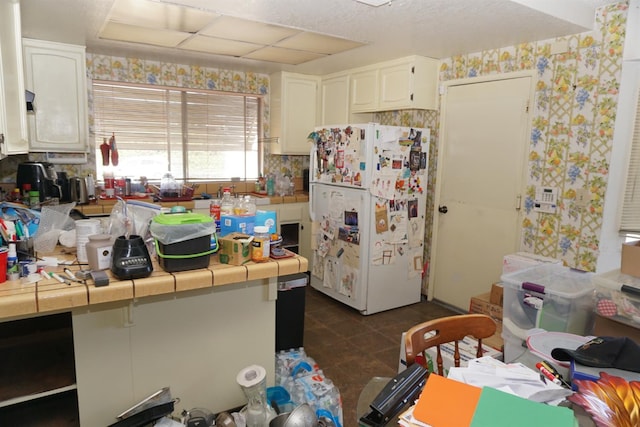 7637 Nixos Way, Sacramento, CA 95823 - kitchen featuring freestanding refrigerator, tile counters, white cabinetry, wallpapered walls, and dark tile patterned flooring