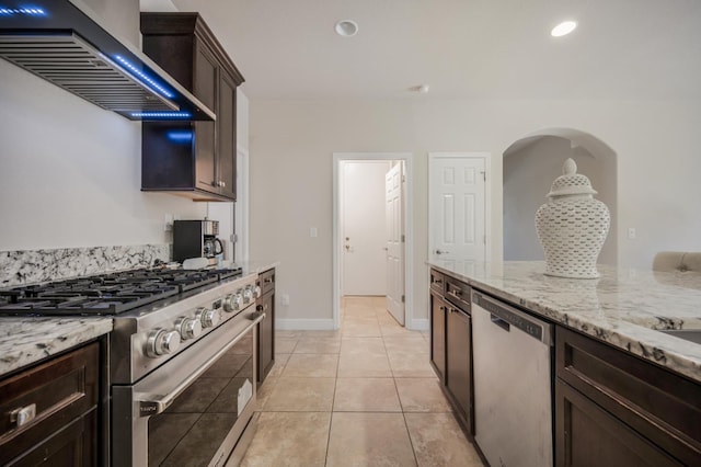 1728 E Green Sage Ave, Fresno, CA 93730 - kitchen featuring appliances with stainless steel finishes, wall chimney exhaust hood, dark brown cabinets, light stone countertops, and light tile patterned floors
