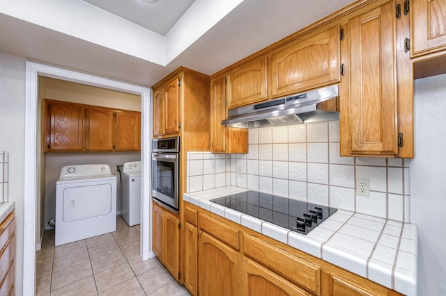 6283 N Gilroy Ave, Fresno, CA 93722 - kitchen featuring black electric stovetop, under cabinet range hood, stainless steel oven, washer and dryer, and tile counters
