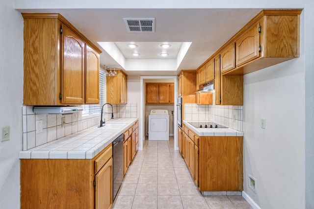 6283 N Gilroy Ave, Fresno, CA 93722 - kitchen with washer / clothes dryer, under cabinet range hood, black appliances, a raised ceiling, and tasteful backsplash
