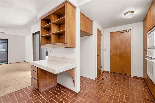 835 E Ashcroft Ave, Fresno, CA 93704 - kitchen with tile countertops, brick patterned flooring, open shelves, white oven, and brown cabinets