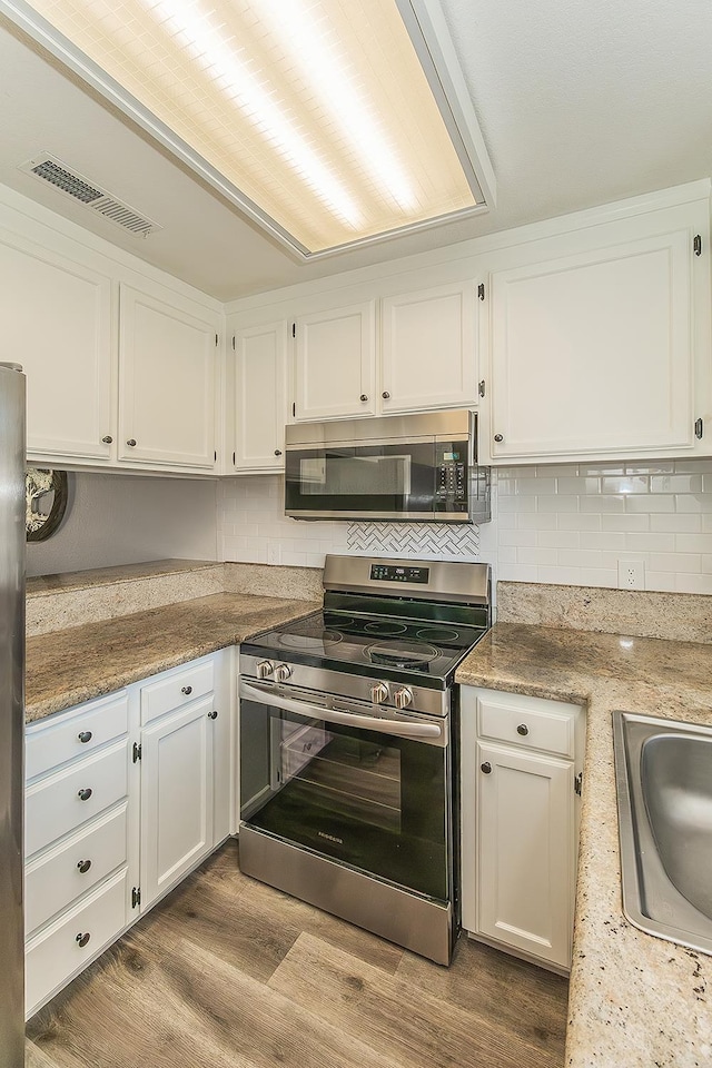 4885 N Backer Ave Unit 113, Fresno, CA 93726 - kitchen featuring appliances with stainless steel finishes, white cabinets, backsplash, and wood finished floors