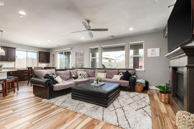 1397 N Redington Ave, Clovis, CA 93619 - living room featuring a textured ceiling, a glass covered fireplace, light wood-type flooring, a ceiling fan, and recessed lighting