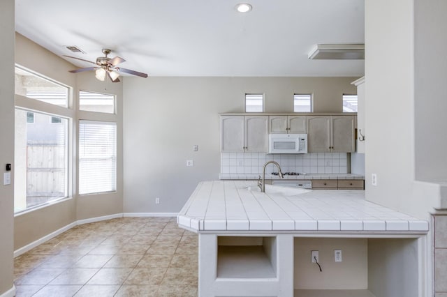 5484 W El Paso Ave, Fresno, CA 93722 - kitchen featuring white microwave, a ceiling fan, tile countertops, backsplash, and healthy amount of natural light
