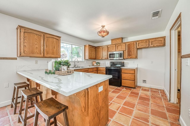 6355 N Cleo Ave, Fresno, CA 93722 - kitchen with electric range, stainless steel microwave, a peninsula, brown cabinetry, and a kitchen breakfast bar