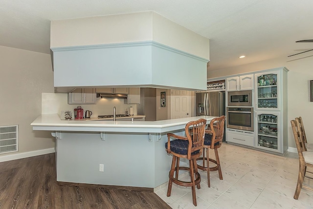 4950 W Minarets Ave, Fresno, CA 93722 - kitchen with stainless steel appliances, under cabinet range hood, a kitchen breakfast bar, a peninsula, and light countertops