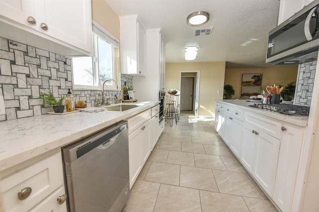 5942 S Cedar Ave, Fresno, CA 93725 - kitchen with appliances with stainless steel finishes, decorative backsplash, white cabinetry, light tile patterned flooring, and light stone counters