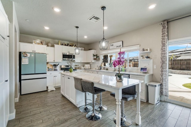 6236 E Garland Ave, Fresno, CA 93727 - kitchen with appliances with stainless steel finishes, white cabinets, wood finished floors, a kitchen island, and recessed lighting