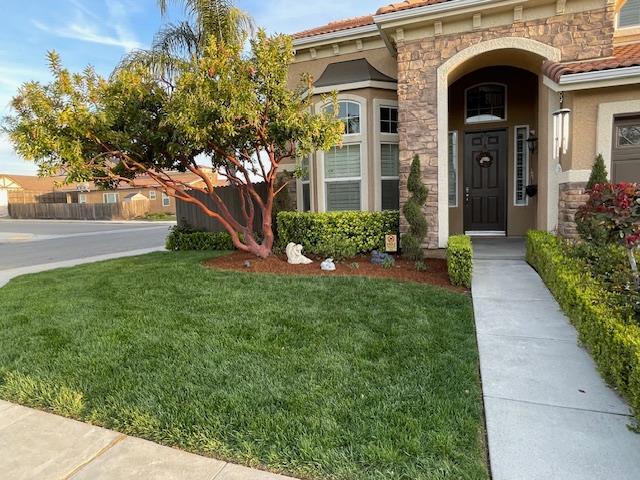 2291 E Prestwick Ave, Fresno, CA 93730 - view of exterior entry featuring stone siding, a yard, stucco siding, and a tile roof