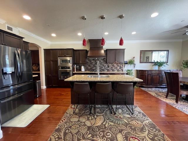 2291 E Prestwick Ave, Fresno, CA 93730 - kitchen featuring appliances with stainless steel finishes, custom range hood, light stone countertops, crown molding, and a breakfast bar