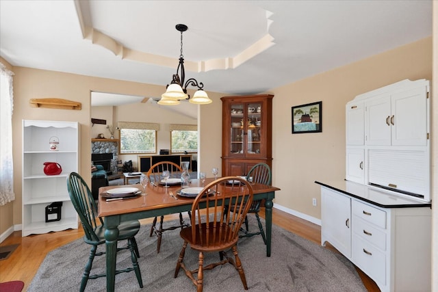 39397 Moonray Ln, Oakhurst, CA 93644 - dining space with light wood-style flooring, a chandelier, a stone fireplace, and a tray ceiling