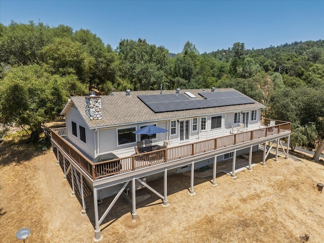 39397 Moonray Ln, Oakhurst, CA 93644 - rear view of house with a shingled roof, a wooden deck, a wooded view, roof mounted solar panels, and a chimney