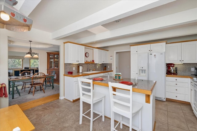 39397 Moonray Ln, Oakhurst, CA 93644 - kitchen with white fridge with ice dispenser, backsplash, white cabinetry, a breakfast bar area, and a kitchen island