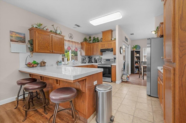 6164 W Keats, Fresno, CA 93723 - kitchen featuring a peninsula, stainless steel appliances, brown cabinetry, a kitchen breakfast bar, and backsplash