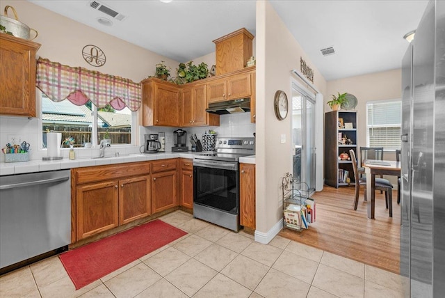 6164 W Keats, Fresno, CA 93723 - kitchen with appliances with stainless steel finishes, tasteful backsplash, under cabinet range hood, light tile patterned floors, and brown cabinets