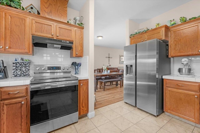 6164 W Keats, Fresno, CA 93723 - kitchen with appliances with stainless steel finishes, tile countertops, under cabinet range hood, tasteful backsplash, and light tile patterned floors