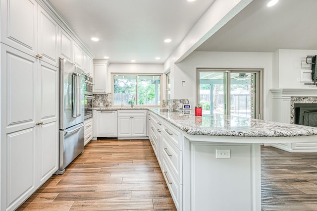 591 E Warwick Ave, Fresno, CA 93720 - kitchen featuring a peninsula, appliances with stainless steel finishes, light wood finished floors, light stone countertops, and white cabinets